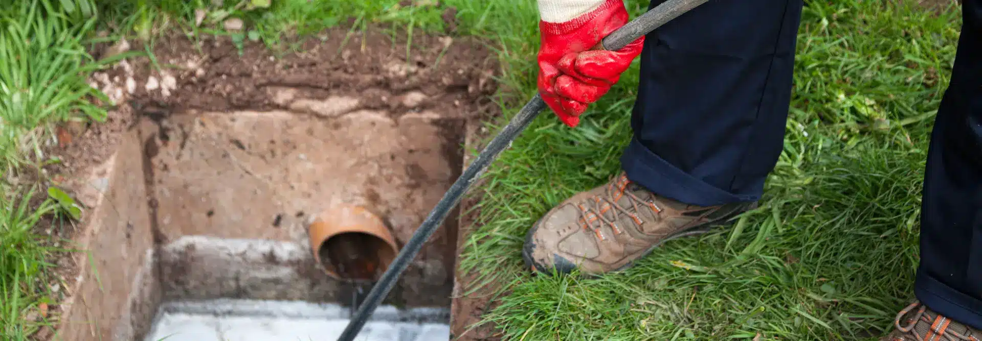 Person cleaning out clogged pipes in lawn