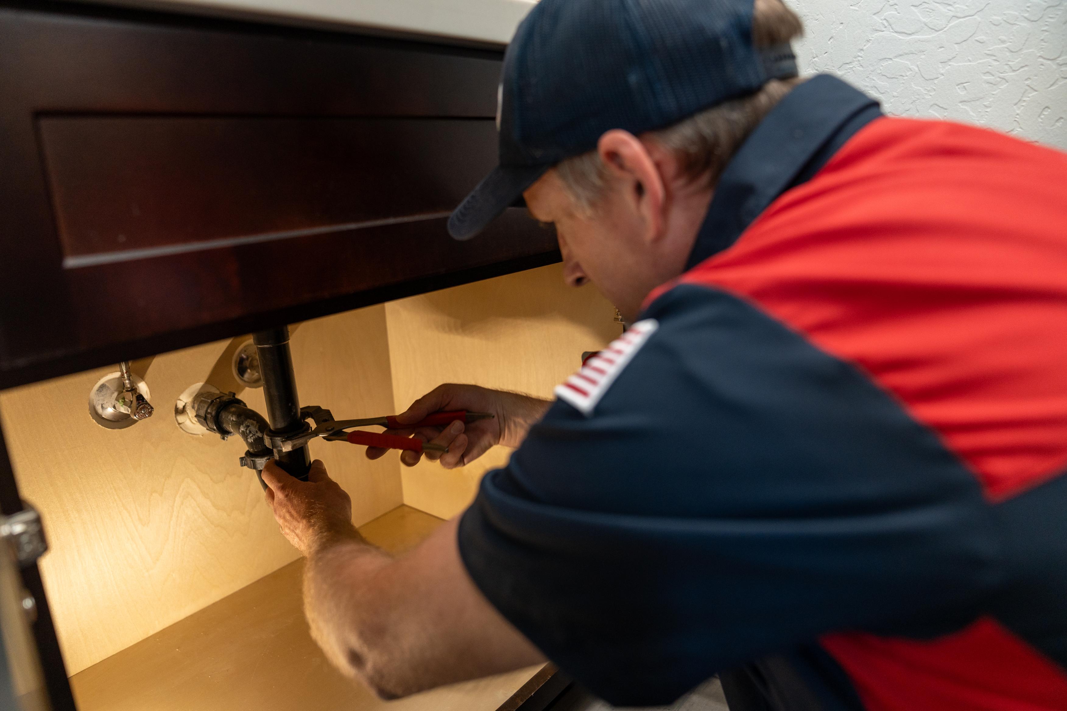 Goettl plumber working on a p-trap under bathroom sink.